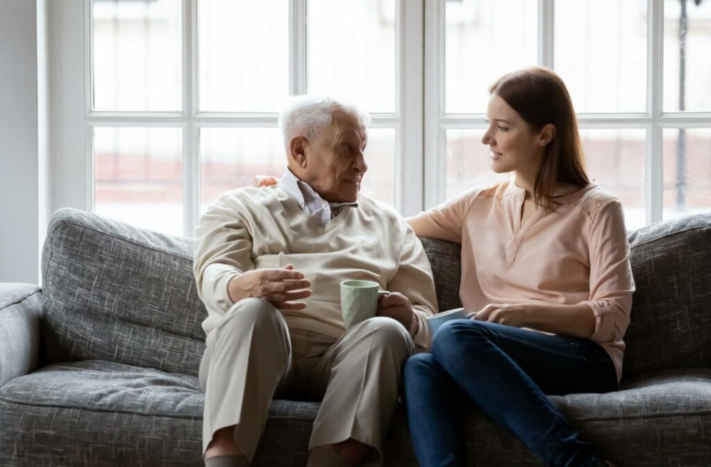 A young woman and older man sitting on a couch looking at each other and having a conversation