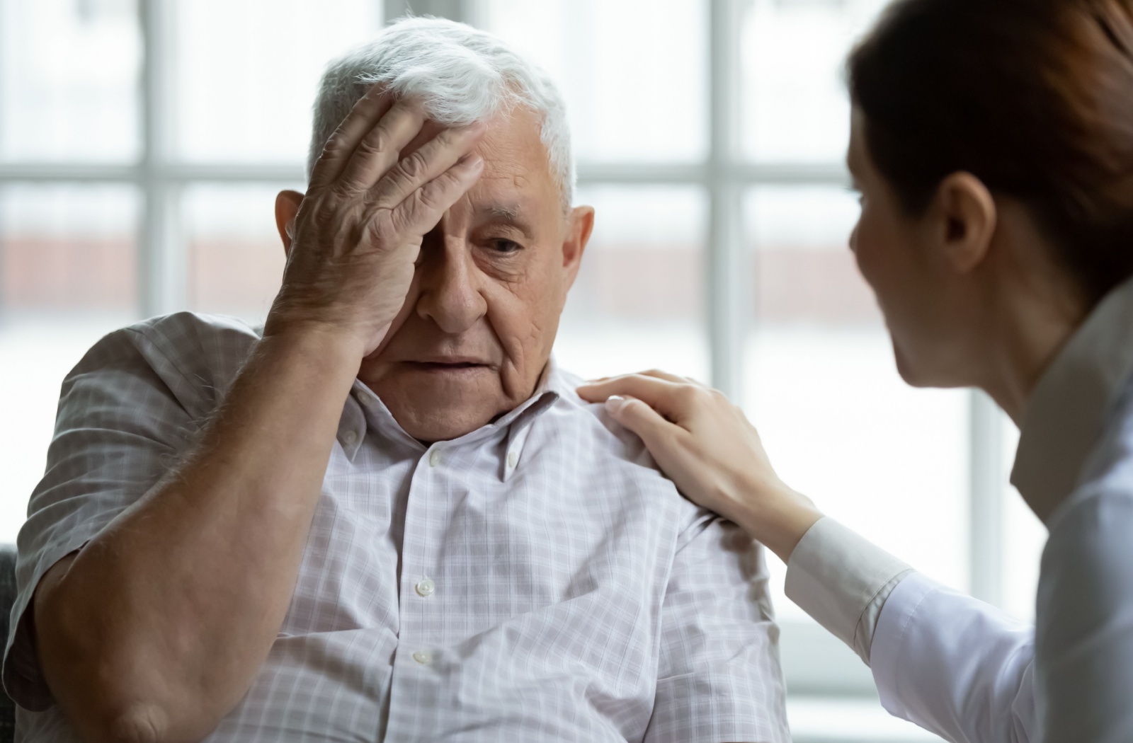 An older adult man with a confused expression having a conversation with a nurse.