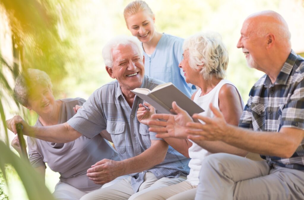 A group of older adults laughing while reading a book at a senior living community. 