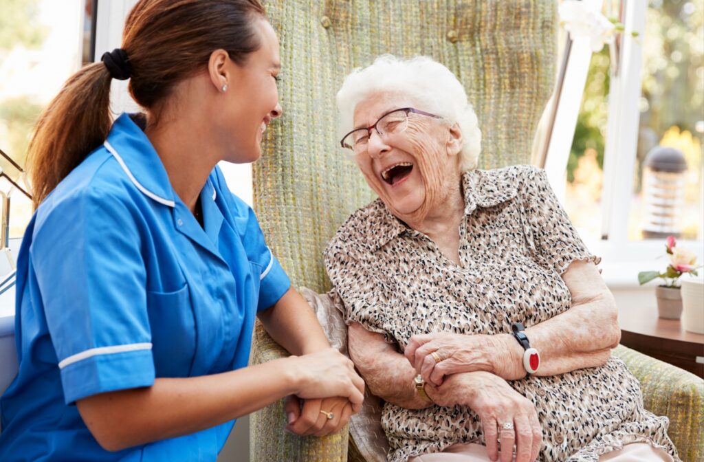 An older woman in a memory care community sitting and laughing while having a conversation with a staff member.