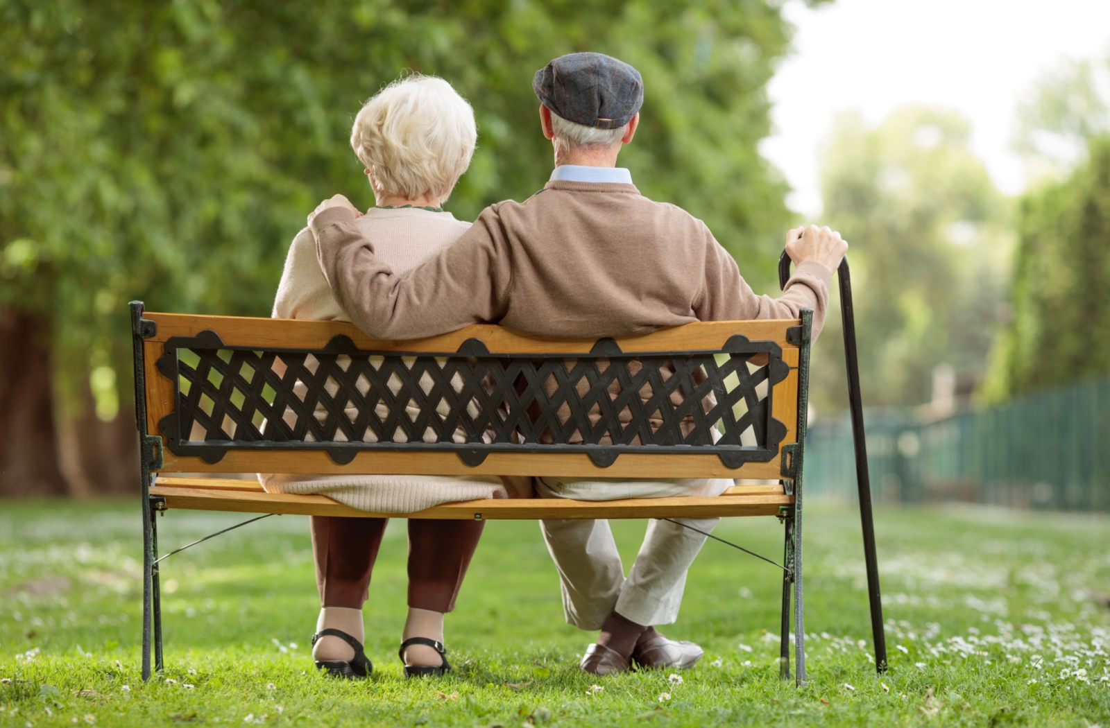 An older couple sitting on a bench in a park.