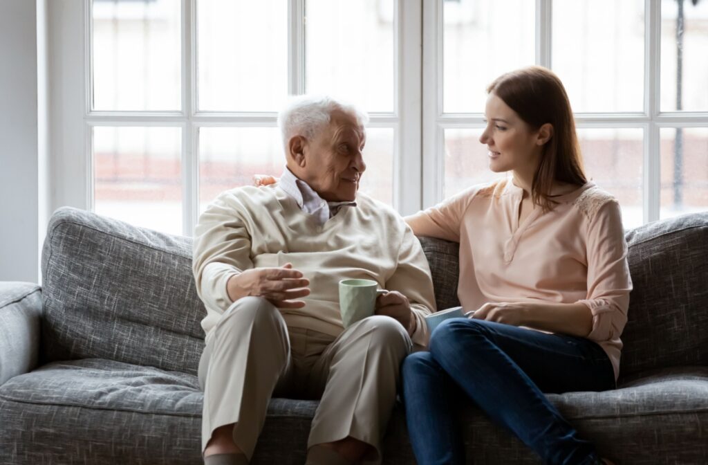 A young woman and older man sitting on a couch looking at each other and having a conversation.