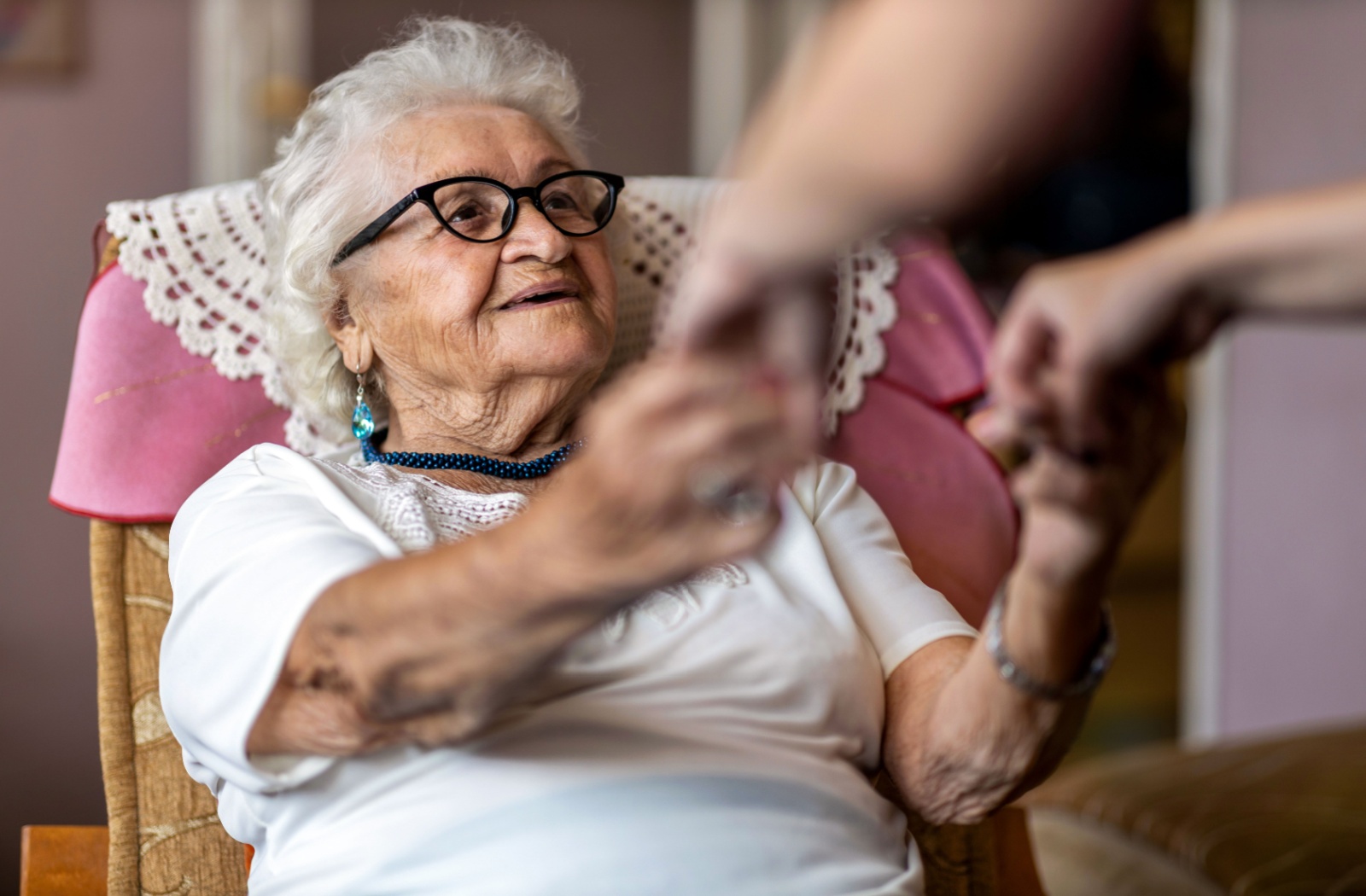 An elderly woman holding hands with her caregiver.