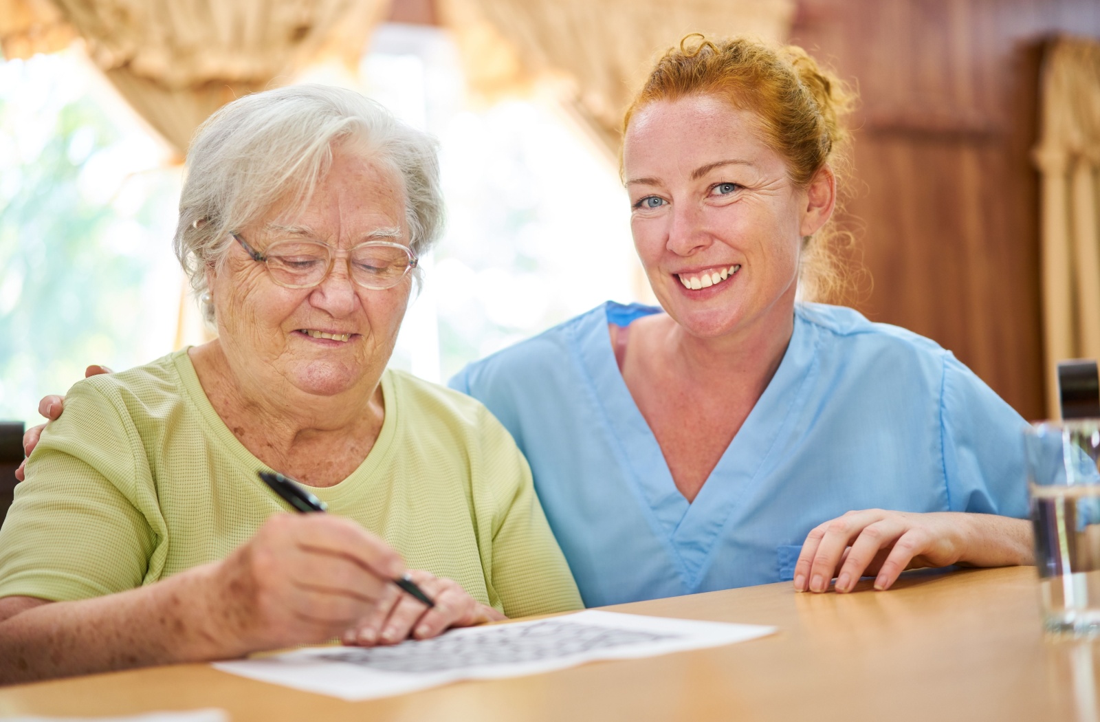 A memory care worker assists a resident with a crossword puzzle.