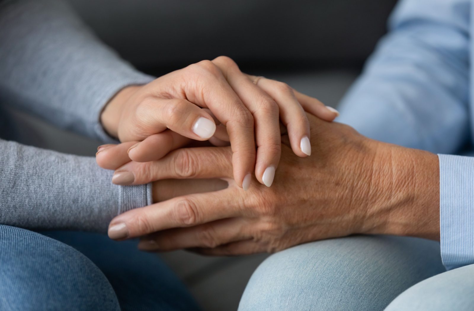 A close-up image of an adult child holding their older parent's hands.