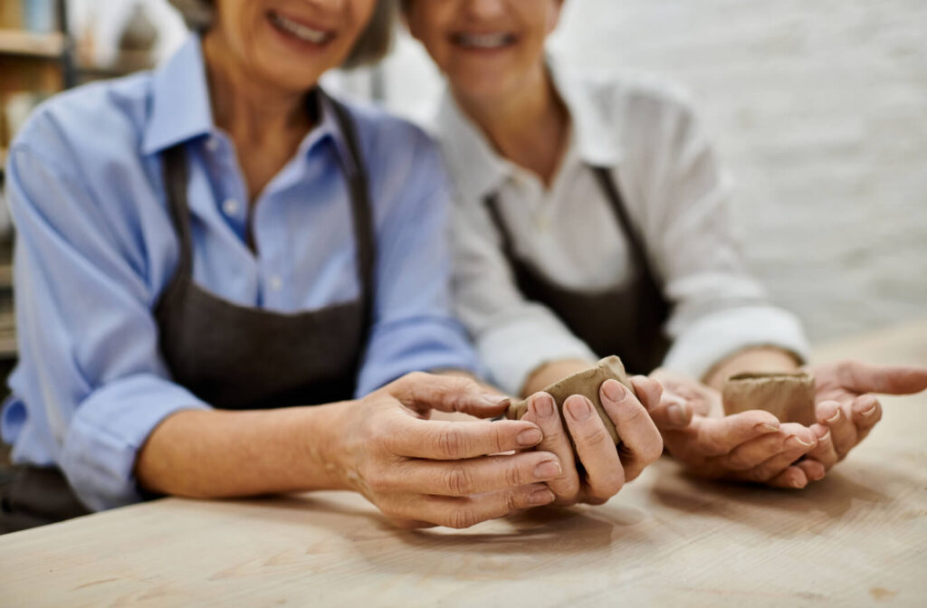 2 older adults with dementia smiling while comparing bowls during a sculpting class.