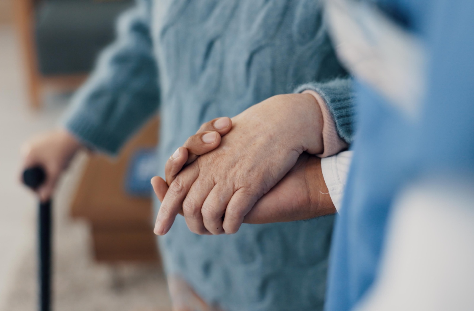 A close-up image of a caregiving holding an older adult's hands as they walk together through memory care