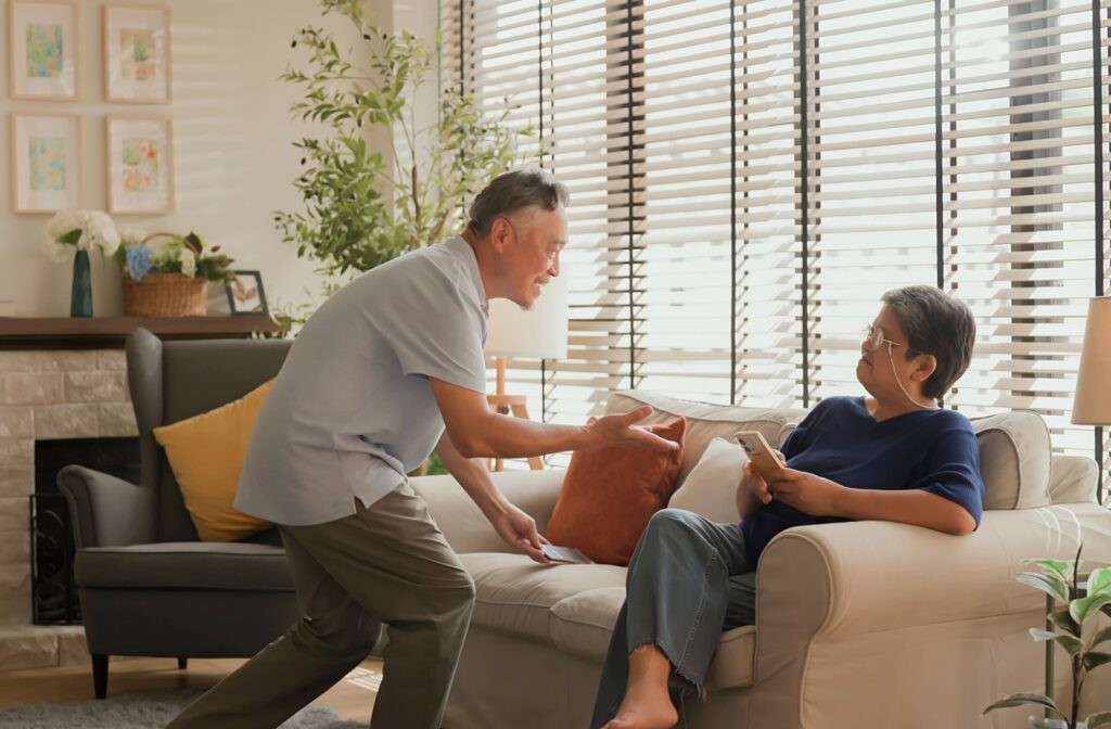 A senior offers their partner a hand to get up to prevent falls in their comfortable, memory care apartment