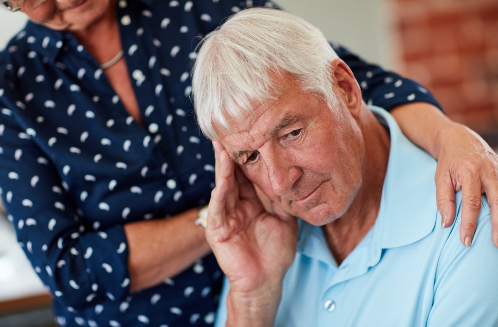 A senior is comforted by their spouse while experiencing memory problems.